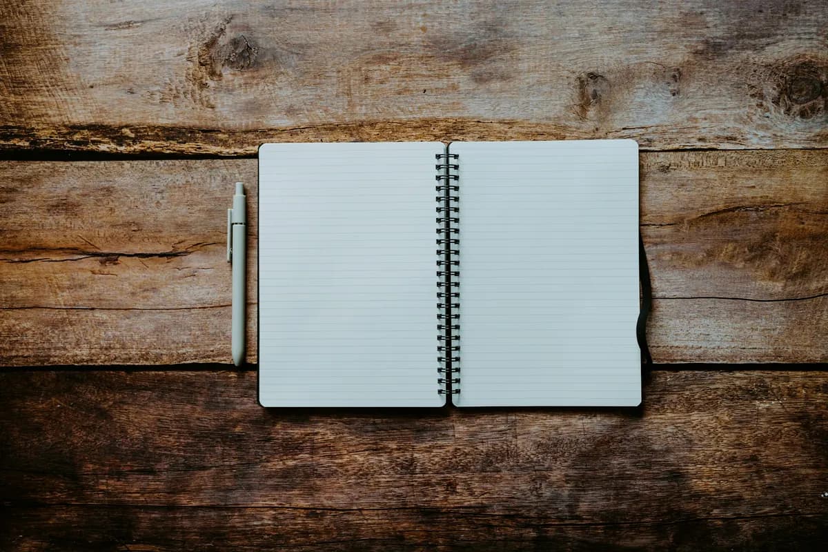 An open spiral notebook with blank lined pages and a pen, lying on a rough wooden table