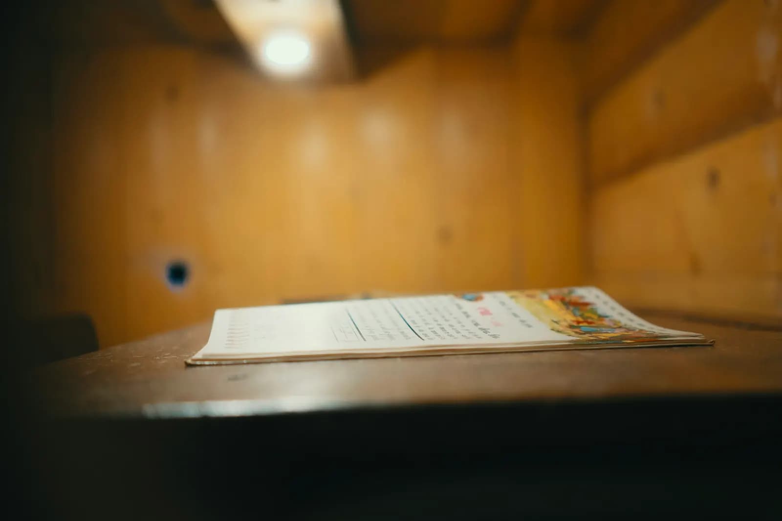 A printed worksheet lying open on a wooden desk under a small ceiling light