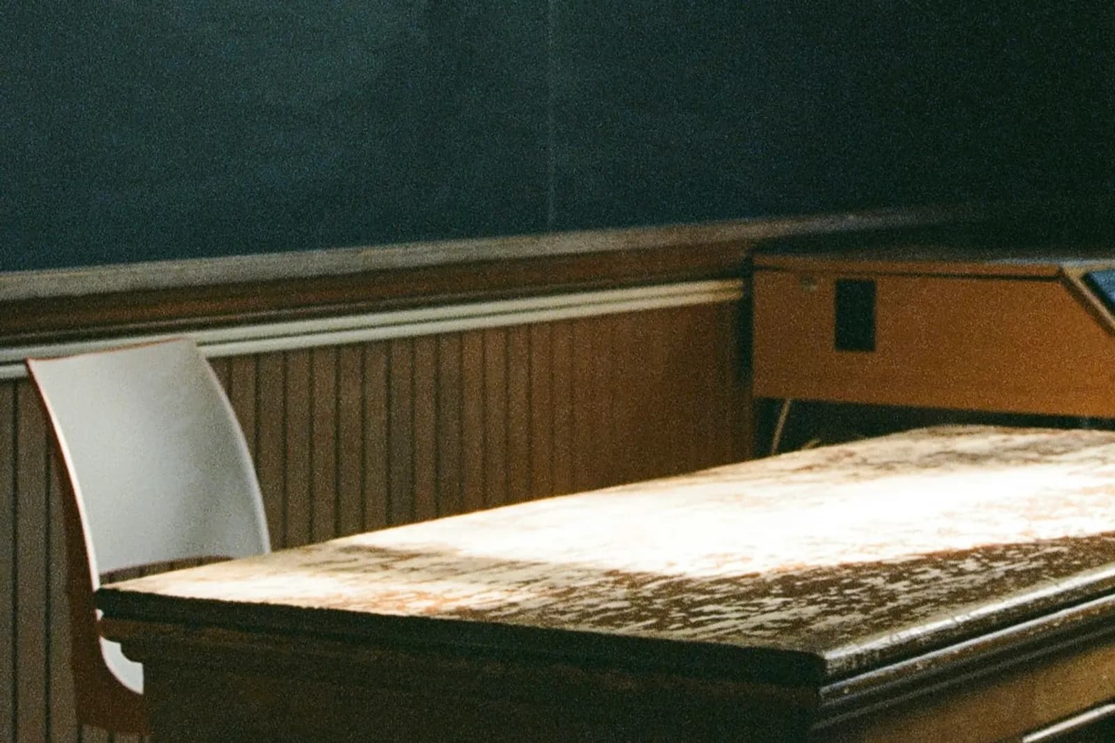 A teacher's wooden desk and chair in front of a blackboard in an empty classroom