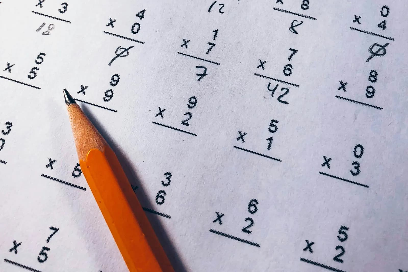A page of multiplication sums worked out in pencil, with a sharpened pencil resting across it